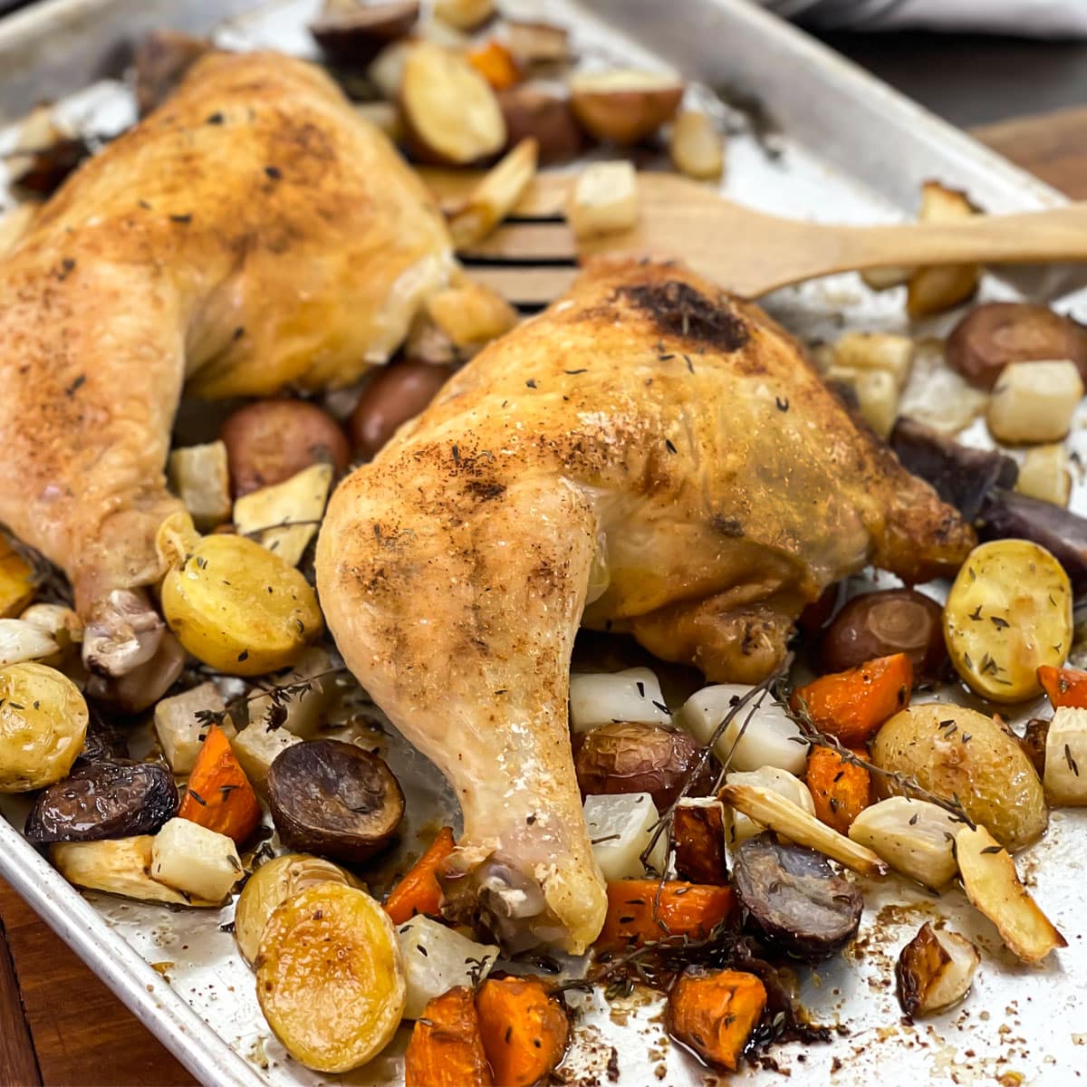 Chicken leg quarters and root vegetables on a sheet pan.