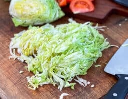 Shredded iceberg lettuce on a wooden cutting board with knife.