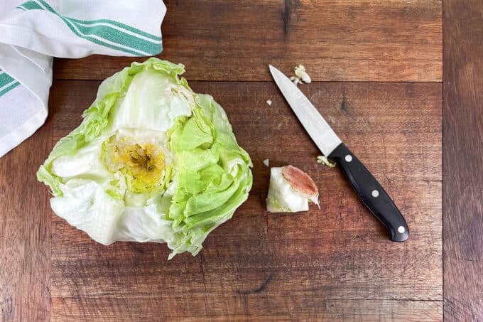 Head of iceberg lettuce with the core cut out, laying beside with paring knife.