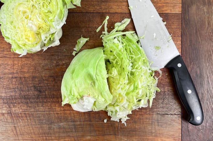 Head of iceberg lettuce on cutting board, half shredded.