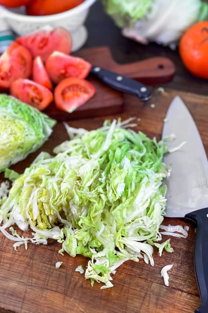 Shredded iceberg lettuce on a wooden cutting board with knife.