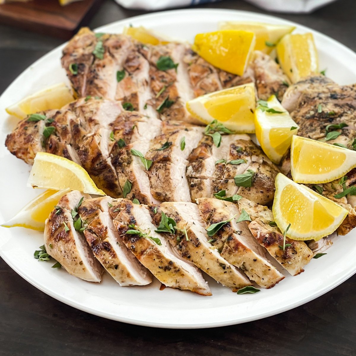 White platter of grilled and sliced chicken breasts with lemon wedges.