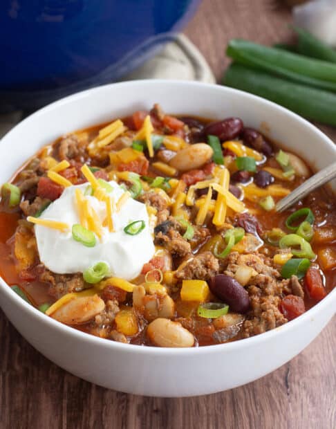 Ground turkey chili in white bowl topped with sour cream, cheese, and green onion.