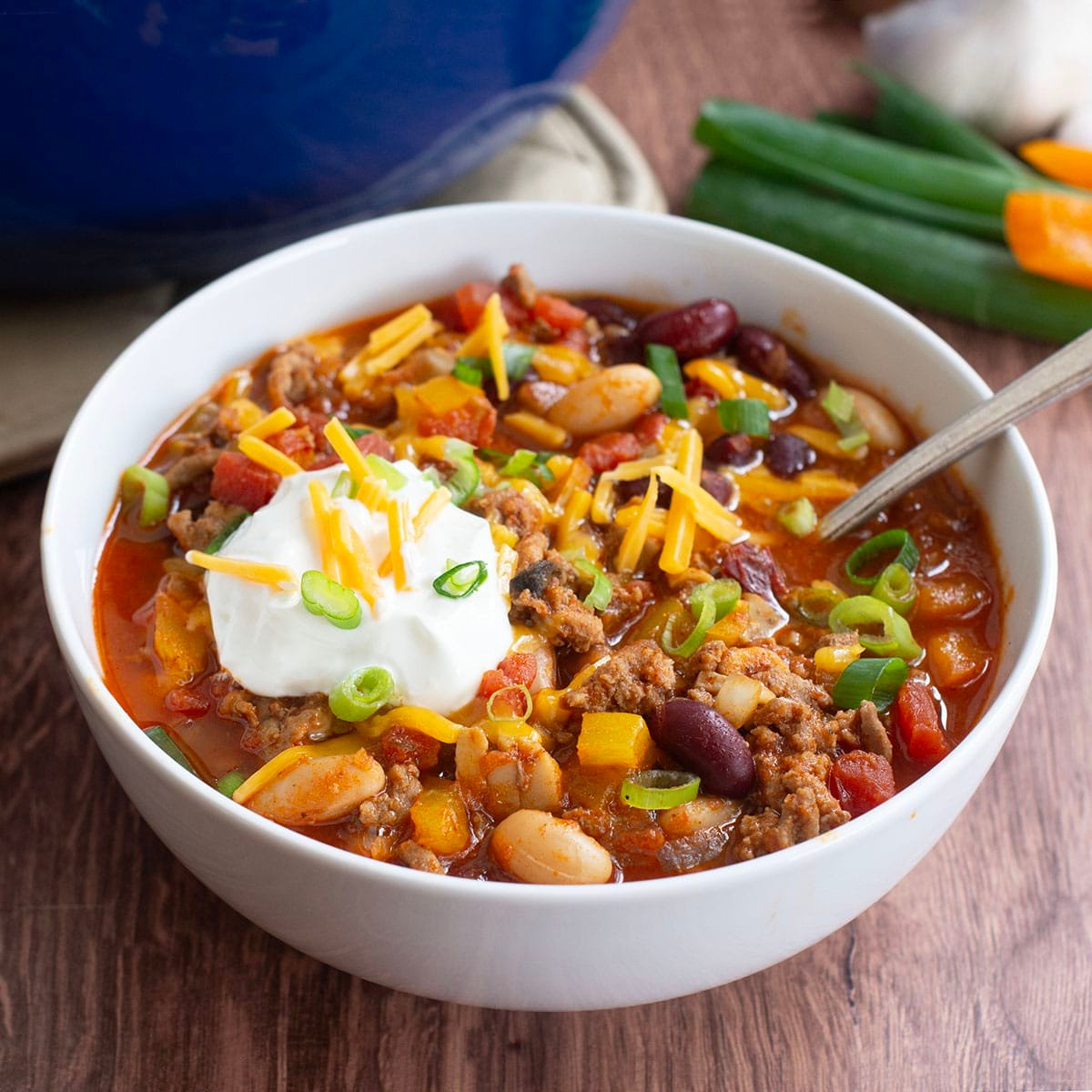 Ground turkey chili in white bowl topped with sour cream, cheese, and green onion.