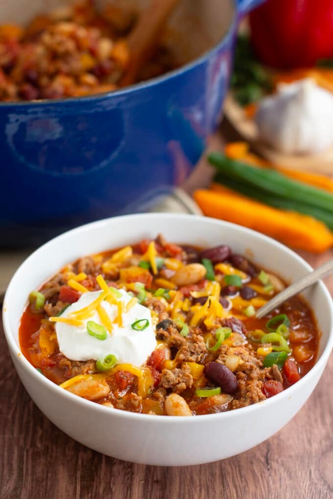 Ground turkey chili in white bowl topped with sour cream, cheese, and green onion.