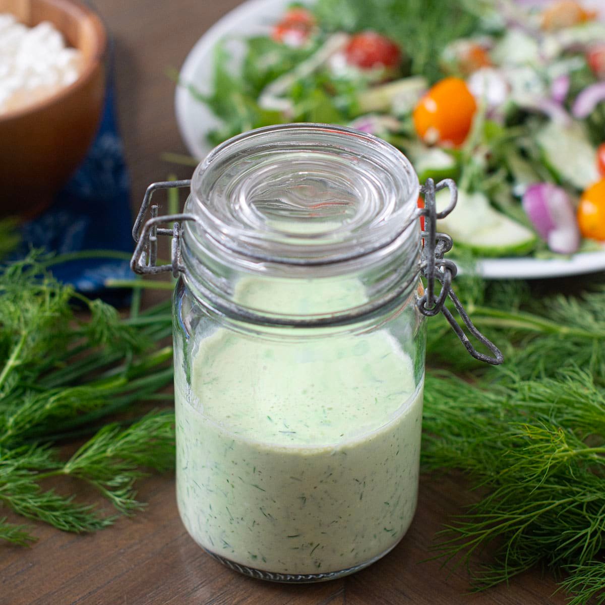 Green Goddess dressing in glass jar. Fresh dill around, salad in background.