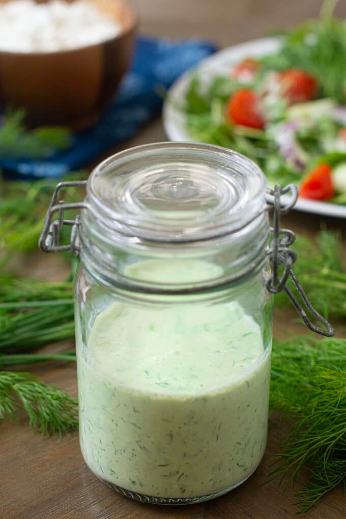 Green Goddess dressing in glass jar. Fresh dill around, salad in background.