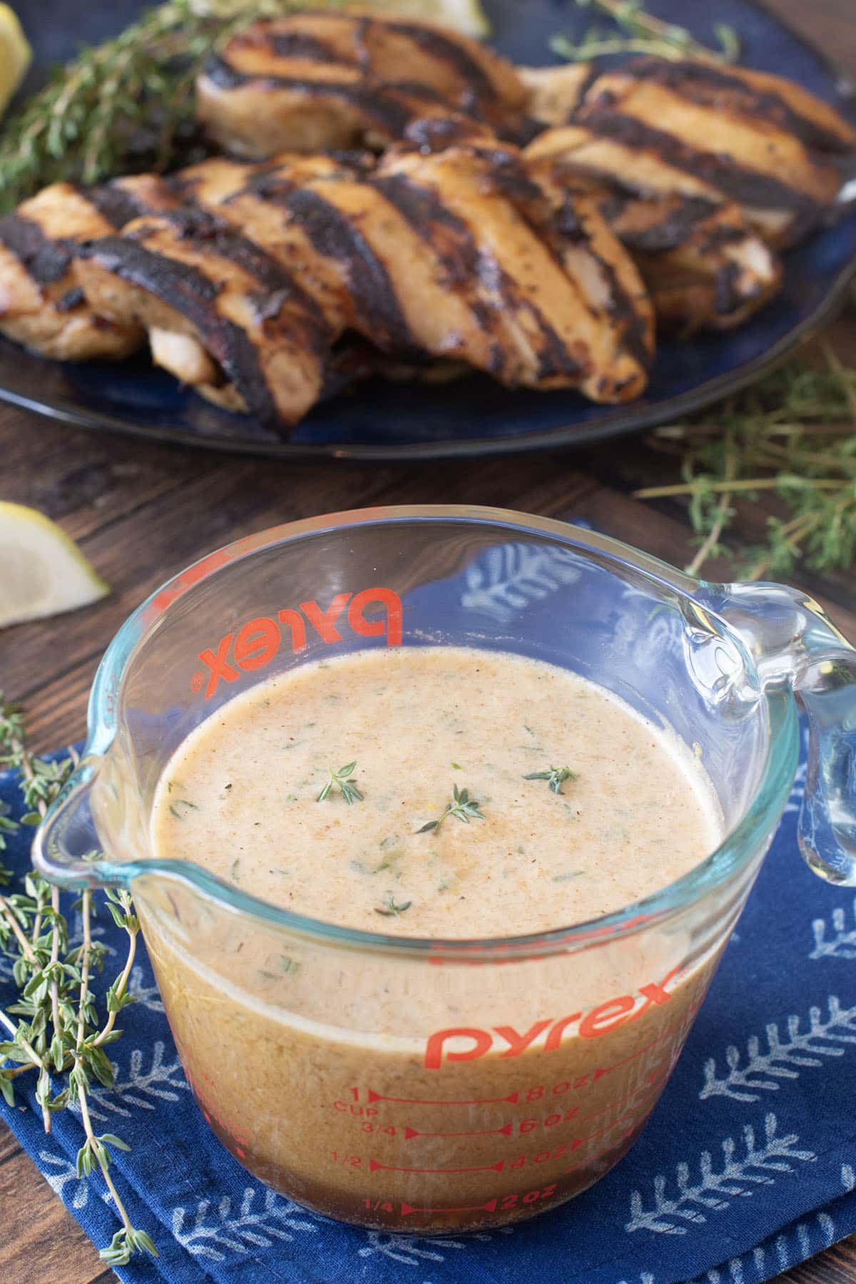 Glass measuring cup of chicken marinade with grilled chicken in background.