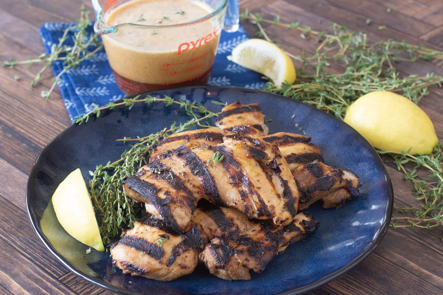 Blue plate of grilled chicken thighs with marinade behind.