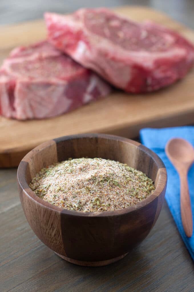 Wooden bowl with Santa Maria seasoning blend, raw beef in background.