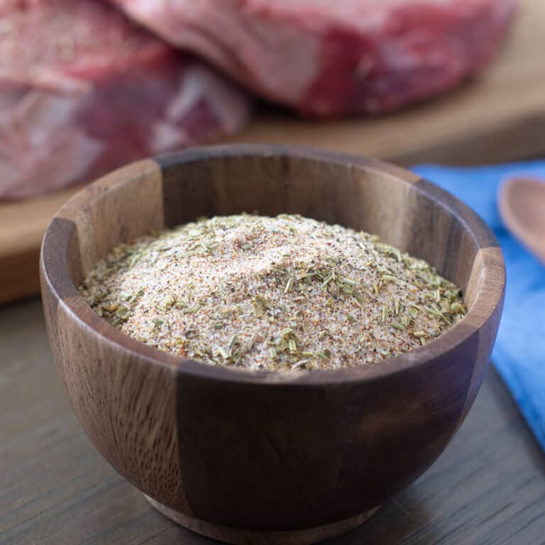 Wooden bowl with Santa Maria seasoning blend, raw beef in background.