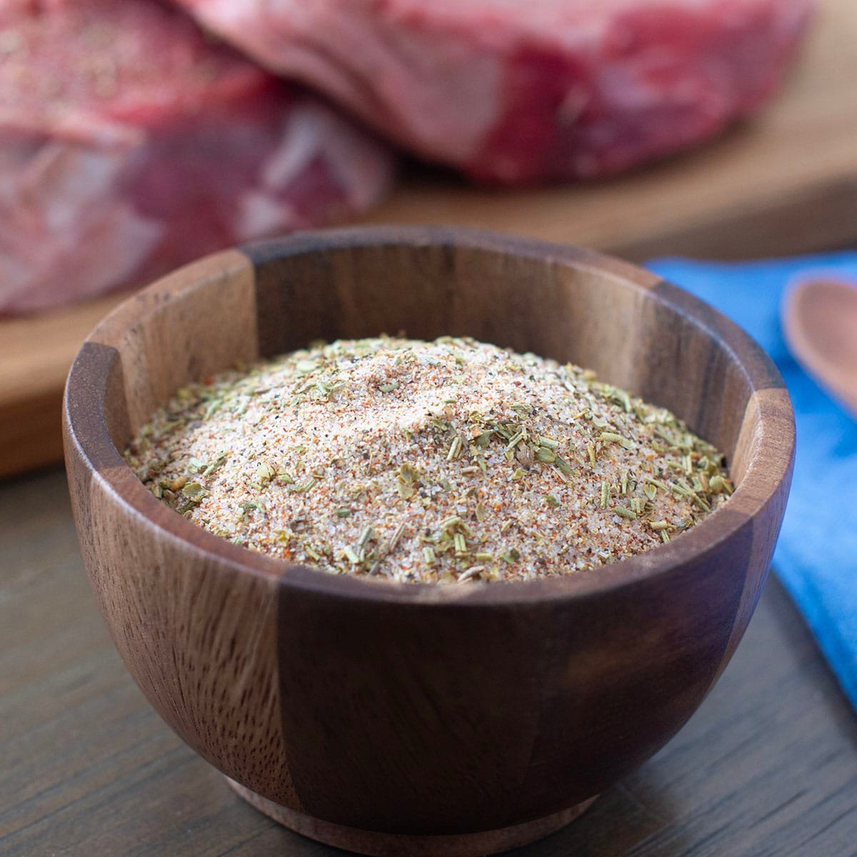 Wooden bowl with Santa Maria seasoning blend, raw beef in background.