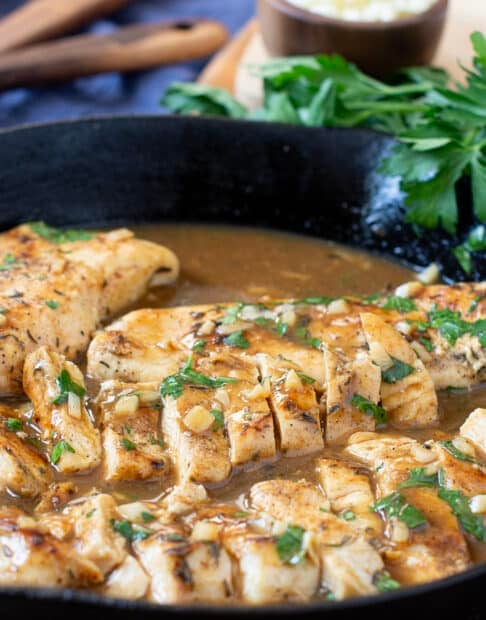 Sliced chicken breasts and garlic butter sauce in skillet.
