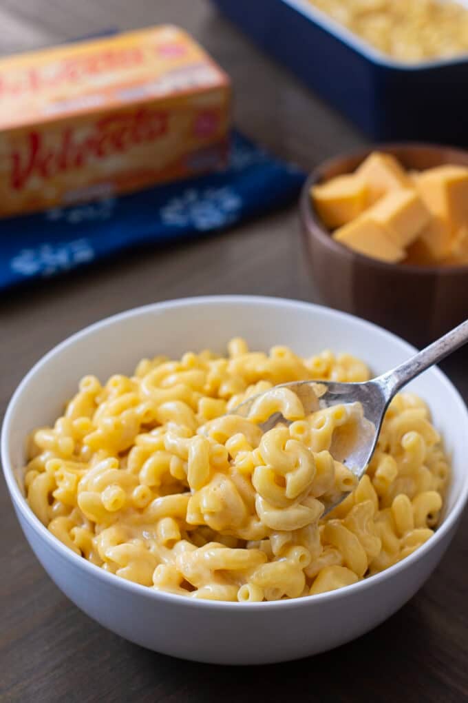 Light gray bowl of Velveeta Mac n Cheese with spoon, block of Velveeta in background.