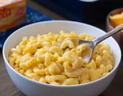 Light gray bowl of Velveeta Mac n Cheese with spoon, block of Velveeta in background.