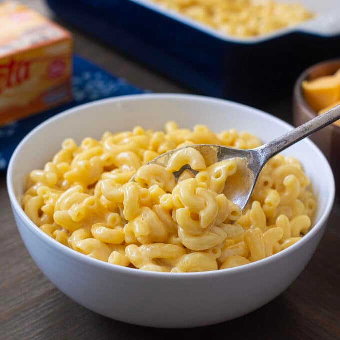 Light gray bowl of Velveeta Mac n Cheese with spoon, block of Velveeta in background.