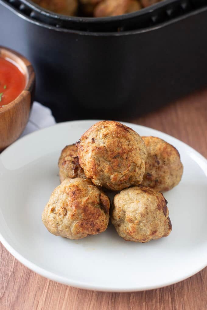 Turkey meatballs on a white plate in front of air fryer.