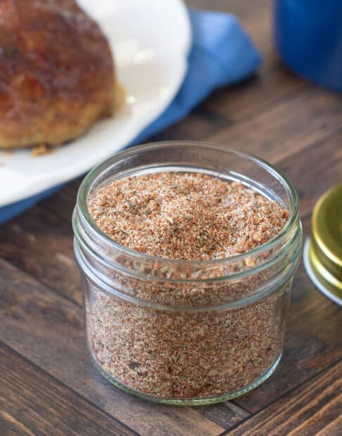 Meatloaf seasoning mix in a glass jar with meatloaf in background.