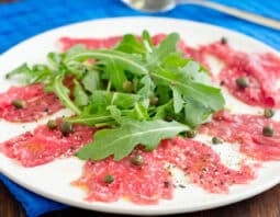 Beef carpaccio with arugula and capers on a white plate.