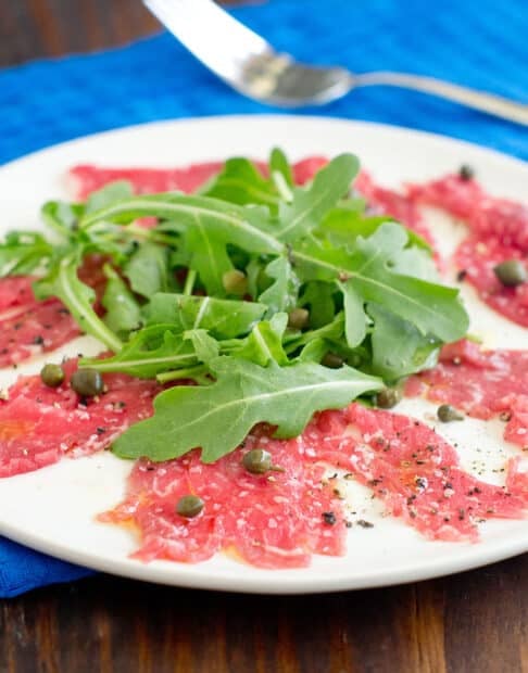 Beef carpaccio with arugula and capers on a white plate.