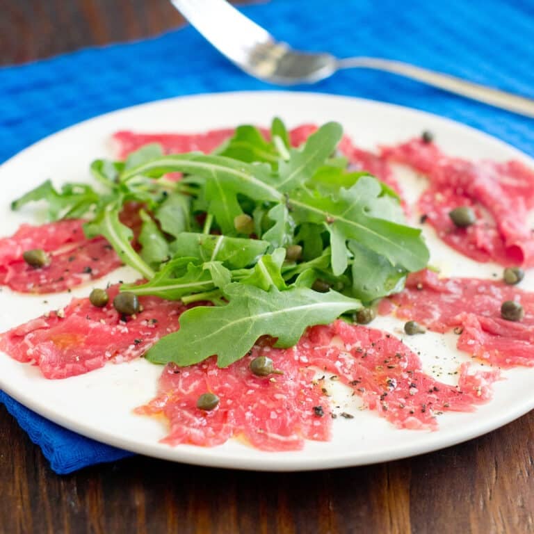 Beef carpaccio with arugula and capers on a white plate.