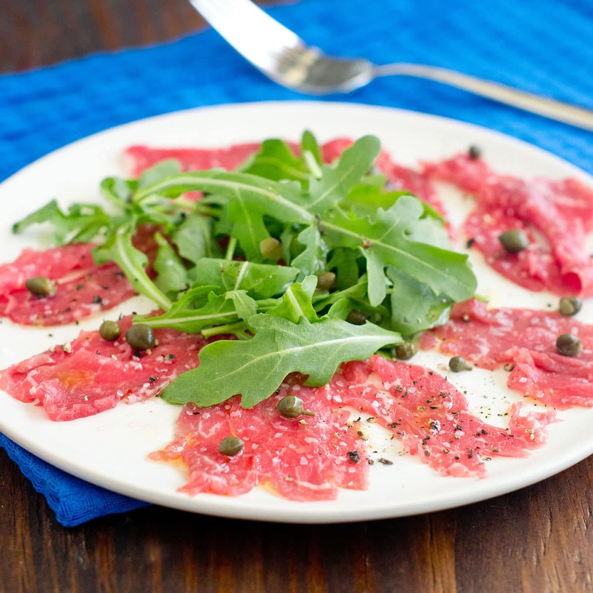 Beef carpaccio with arugula and capers on a white plate.