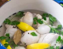 Chicken thighs in a pot with stock, herbs, and lemon wedges.