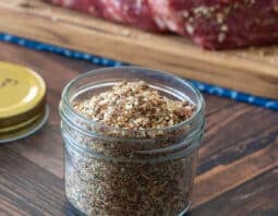 Glass jar with homemade pot roast seasoning, raw roast in background.