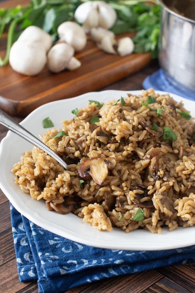 White plate of mushroom rice with fresh mushrooms in background.