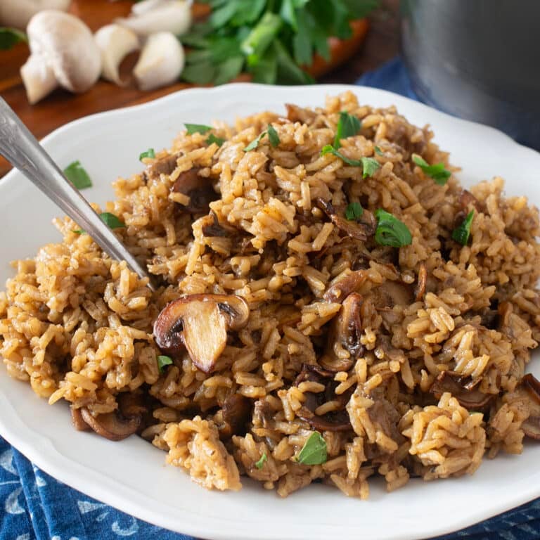 White plate of mushroom rice with fresh mushrooms in background.