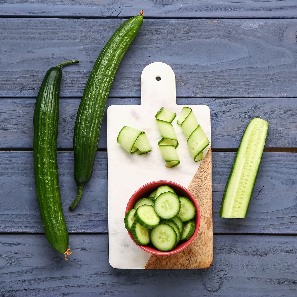 Cucumbers, sliced and curled on a cutting board, whole cucumbers next to.