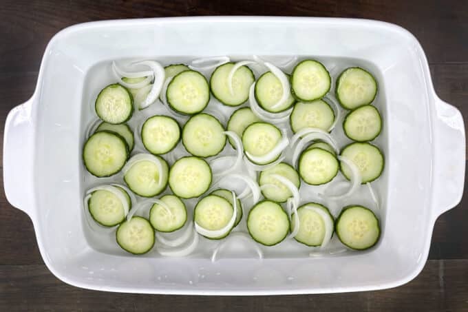 Cucumber slices and onions marinating in vinegar mixture in white dish.