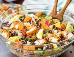 Large glass bowl of crispy chicken salad with wooden serving spoons.