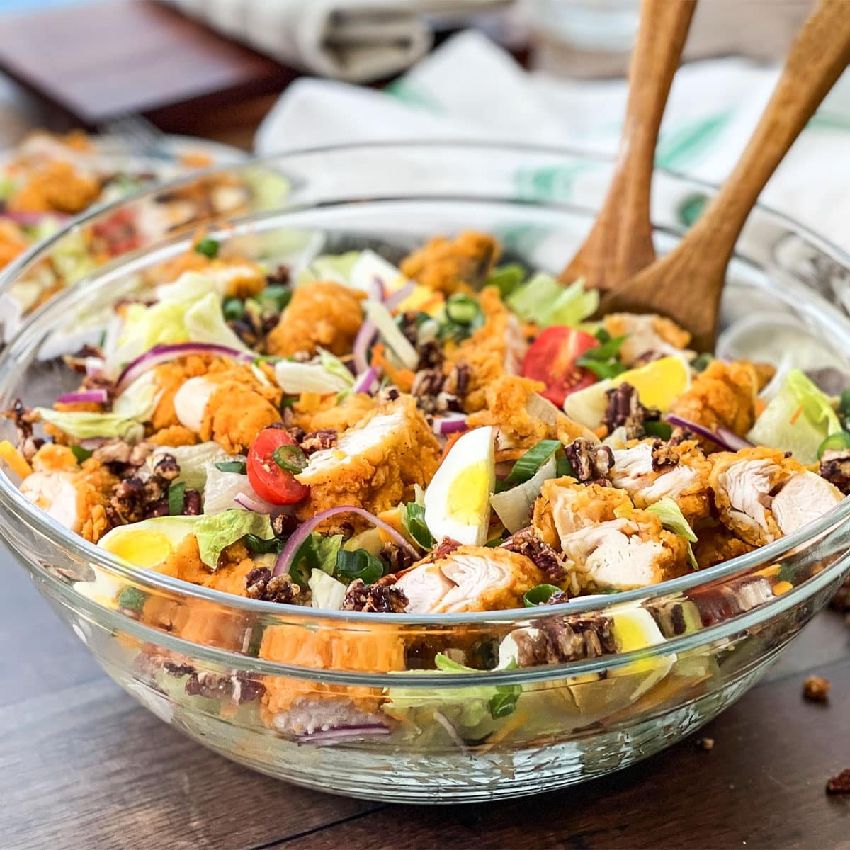 Large glass bowl of crispy chicken salad with wooden serving spoons.