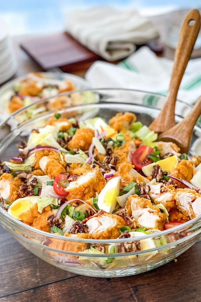 Large glass bowl of crispy chicken salad with wooden serving spoons.