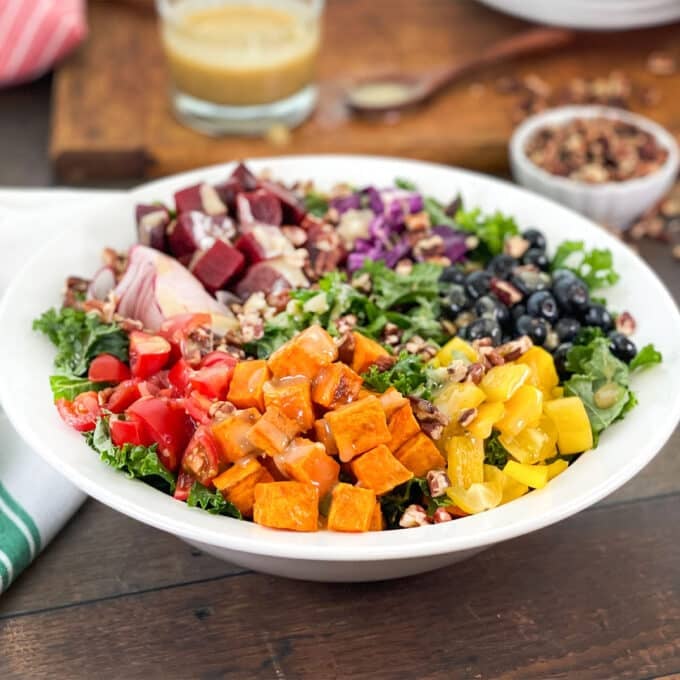 Salad in a white serving bowl with sweet potato, tomatoes, blueberries and more over kale.