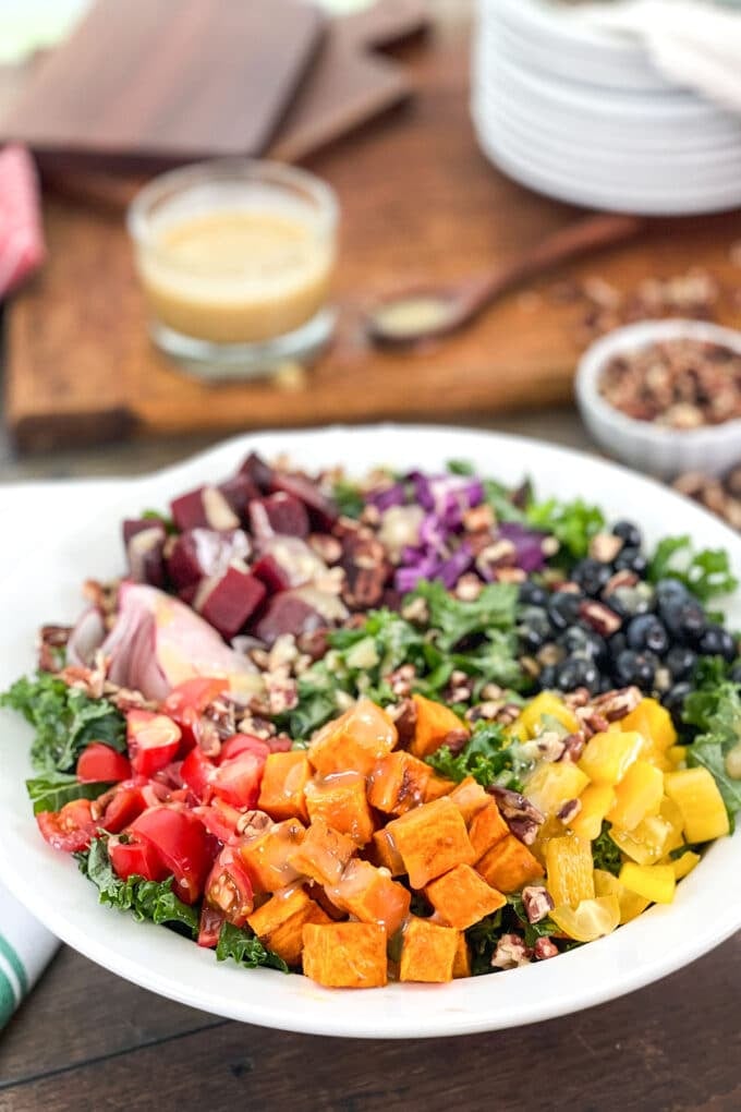 Salad in a white serving bowl with sweet potato, tomatoes, blueberries and more over kale.