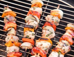 Wooden skewers on a grill with chicken, peppers, and onion.