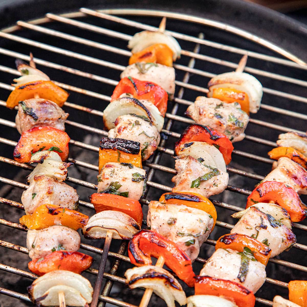 Wooden skewers on a grill with chicken, peppers, and onion.