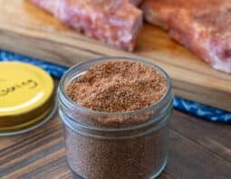 Small glass jar of pork chop seasoning blend with raw pork chops in background.