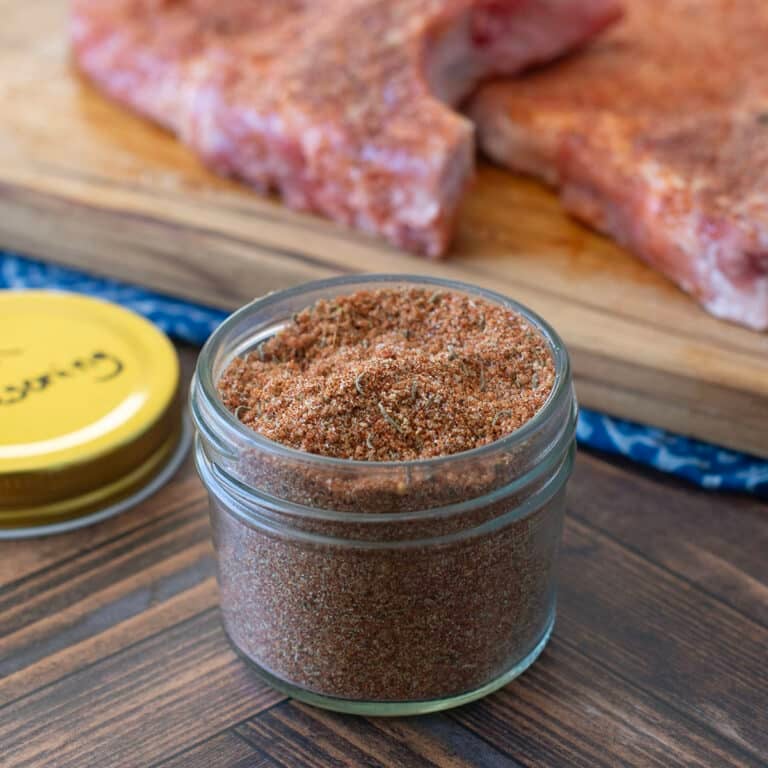 Small glass jar of pork chop seasoning blend with raw pork chops in background.