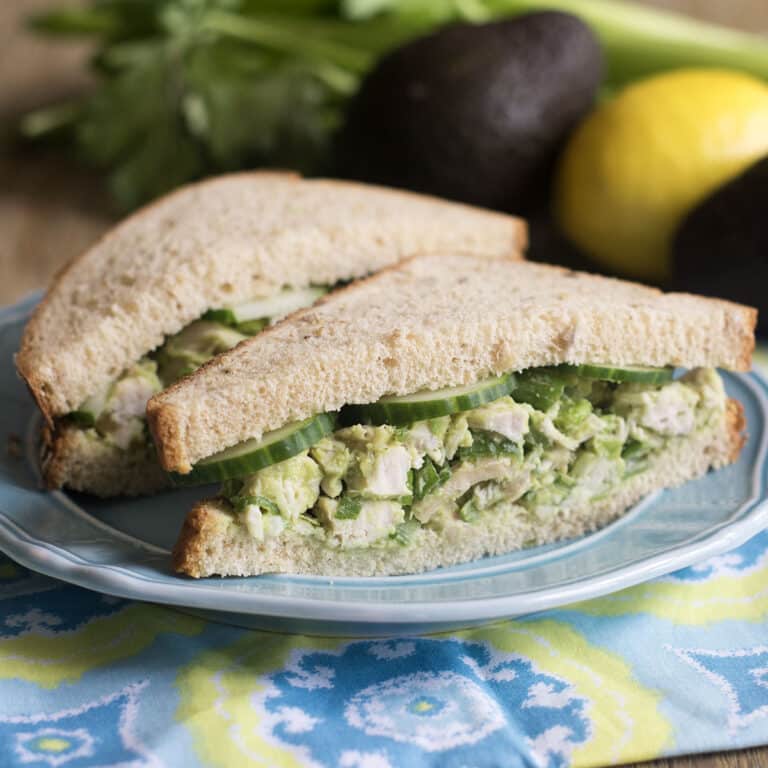 Avocado chicken salad sandwich cut in half on a blue plate.