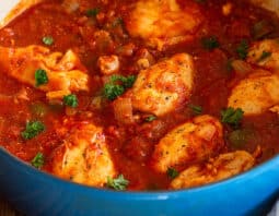 Blue Dutch oven with chicken thigh cacciatore in rich tomato sauce.
