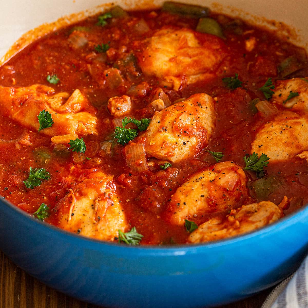 Blue Dutch oven with chicken thigh cacciatore in rich tomato sauce.