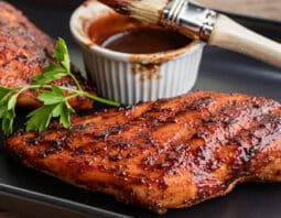 BBQ chicken breasts on a black platter with BBQ sauce dish and basting brush.