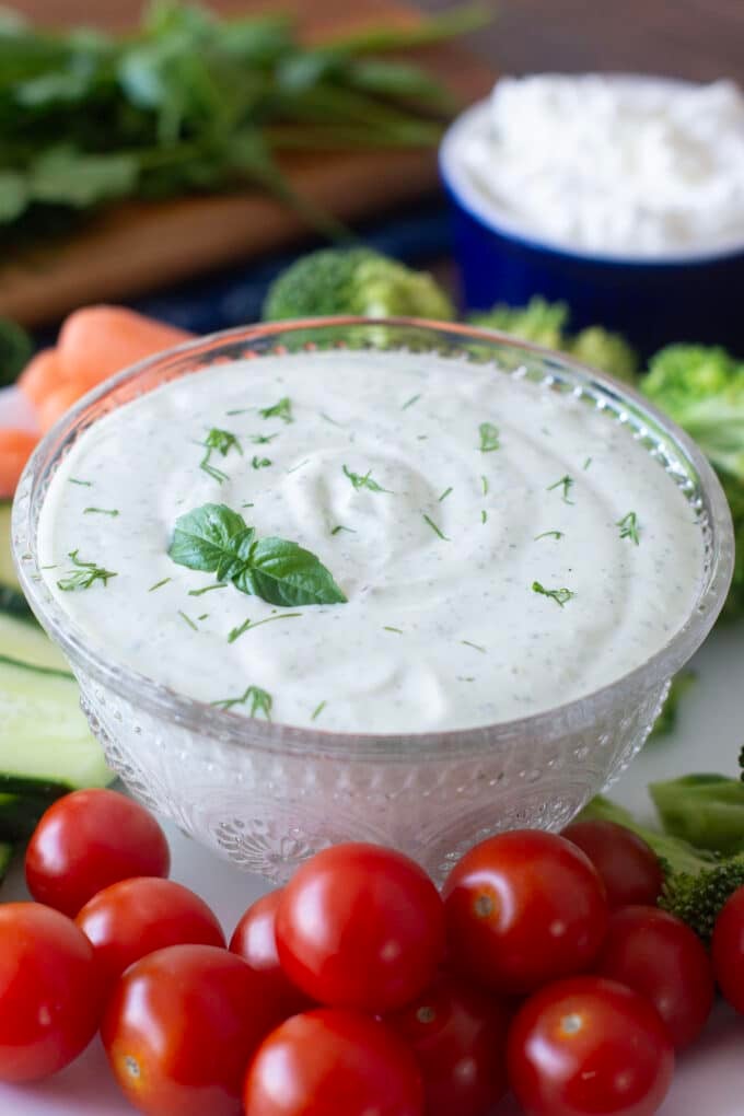 Glass dish of green goddess dip surrounded by fresh veggies.