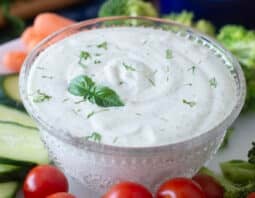 Glass dish of green goddess dip surrounded by fresh veggies.