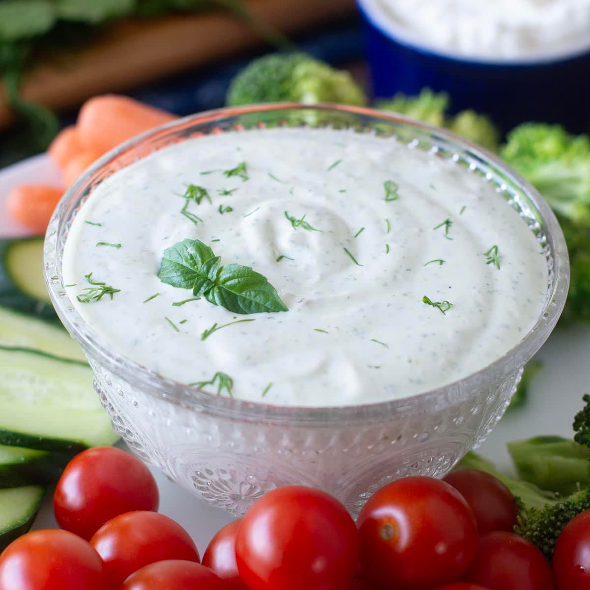 Glass dish of green goddess dip surrounded by fresh veggies.