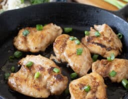 Teriyaki chicken thighs in a cast iron pan topped with green onion.