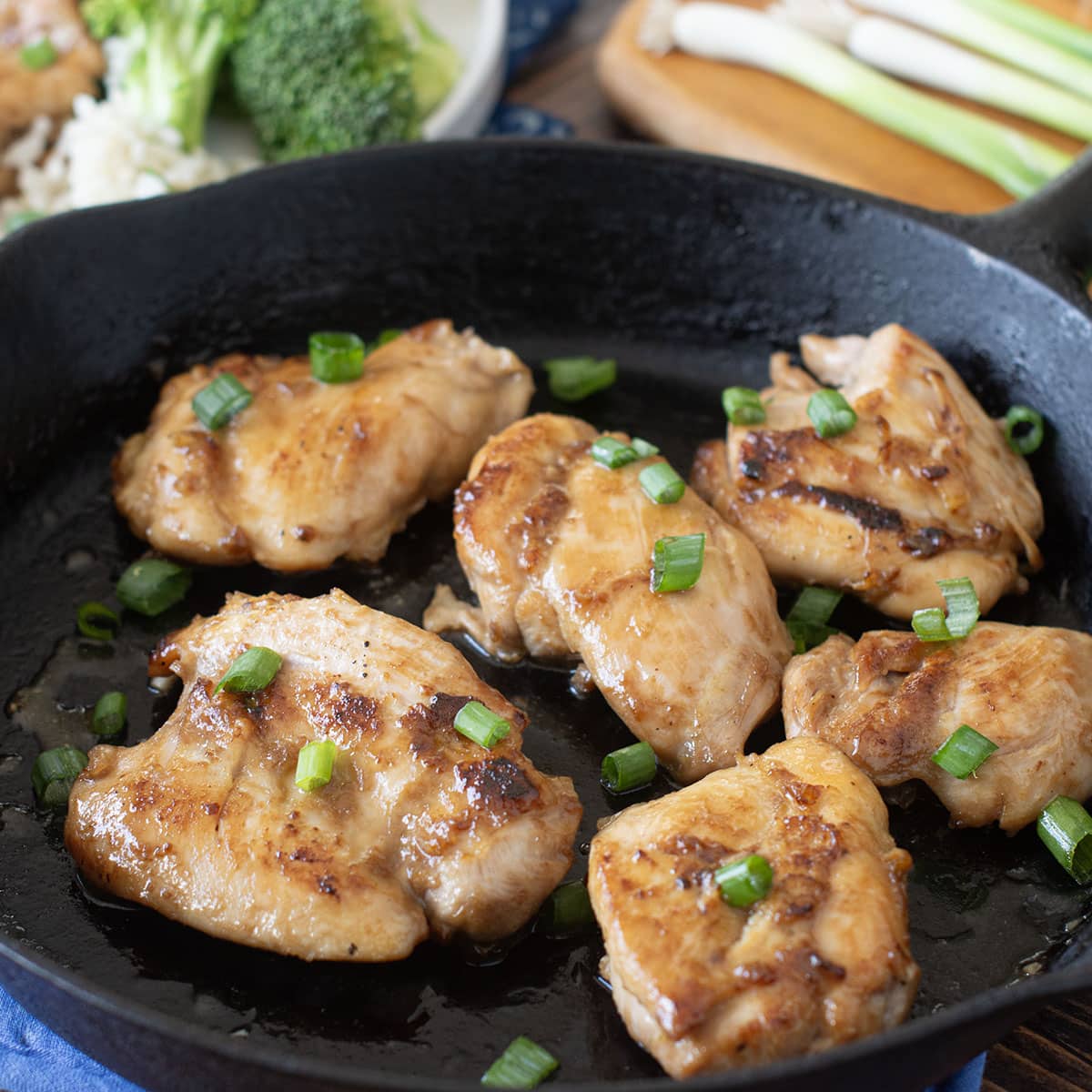 Teriyaki chicken thighs in a cast iron pan topped with green onion.